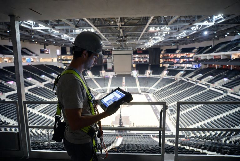 technician using a tablet and inspection tools to assess a large indoor sports arena